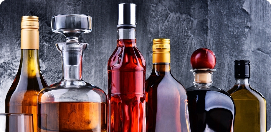 Composition with carafe and bottles of assorted alcoholic beverages.